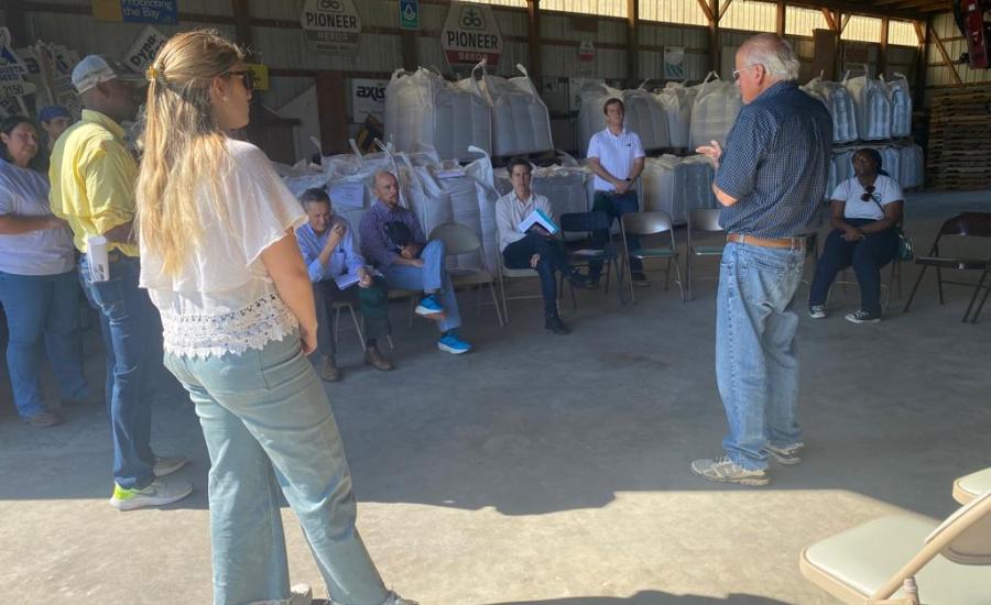 People in a delegation from Argentina, Paraguay, and Uruguay stand in a barn and sit front of bags of cover crop seed while listening to Bobby Hutchison discuss conservation efforts on his 130-year-old family farm.