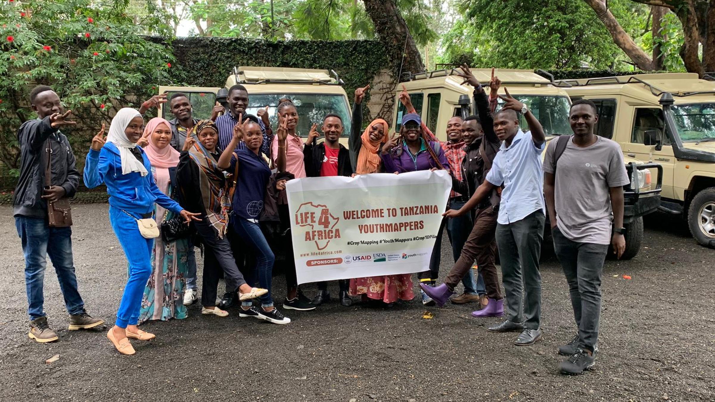 A group of 14 YouthMappers from Tanzania pose in front of jeeps before going out into the field for research